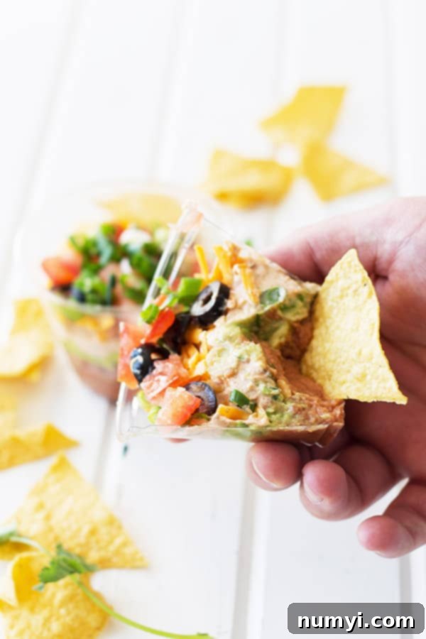 a chip digging some of the taco dip out of a plastic cup