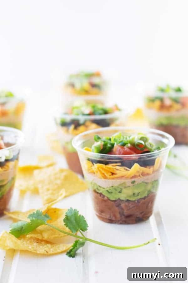 individual seven layer taco dip cups scattered around a table with tortilla chips around