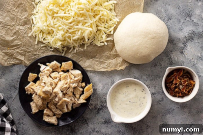 The Ranch Hand's Special 3 Ingredients for Chicken Bacon Ranch Pizza laid out on a table, including pizza dough, cooked chicken, bacon, ranch dressing, and shredded cheese.