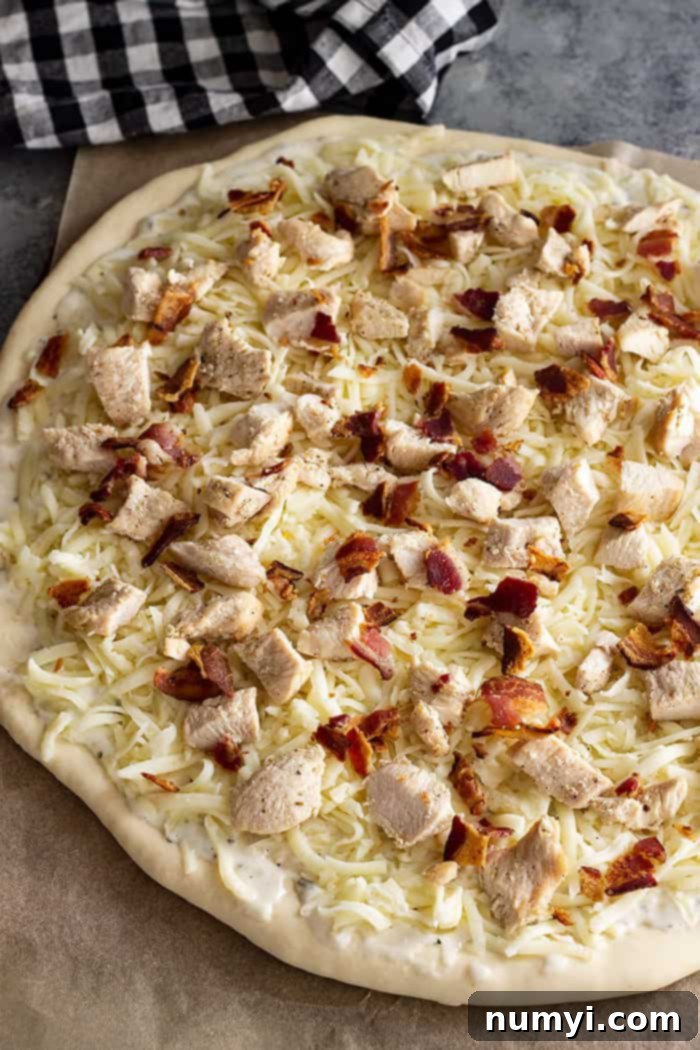 The Ranch Hand's Special 4 A pizza topped with all the ingredients – creamy ranch base, shredded mozzarella, chopped chicken, and crumbled bacon – ready for the oven.