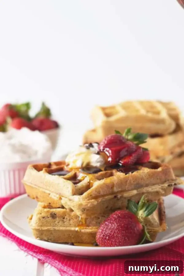 a stack of my recipe for strawberry chocolate chip waffles with syrup, homemade whipped cream, and fresh berries on top, ready for breakfast