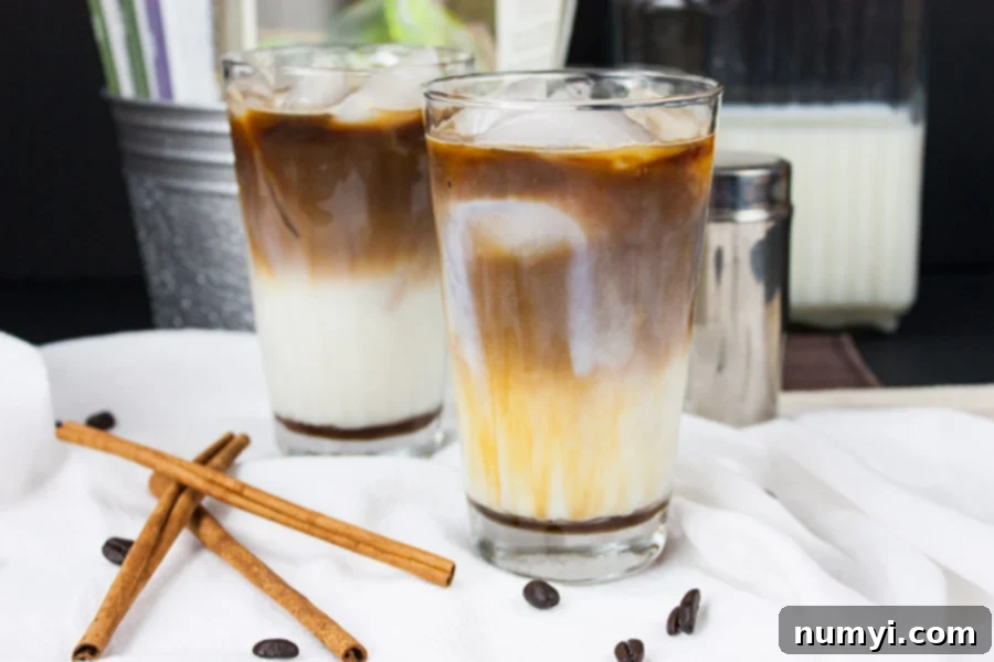 Frosted Cinnamon Macchiato 2 Iced Cinnamon Macchiato with cinnamon sticks and coffee beans laying on a table.
