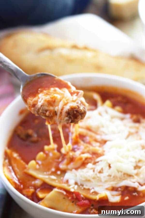 A bowl of lasagna soup with a spoon lifting a bite out, showing the tender noodles, meat, and melted cheese strands.