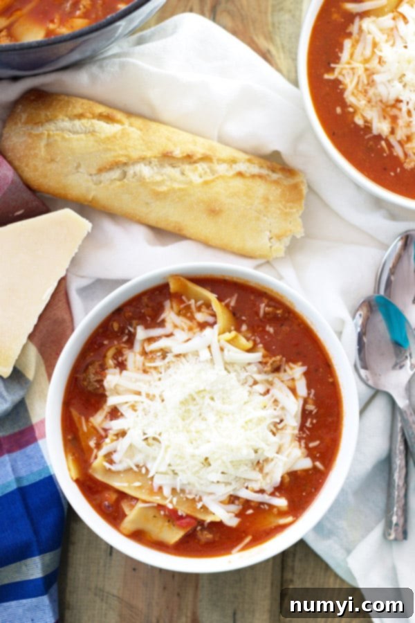 An overhead photo of a bowl of lasagna soup generously topped with cheese, sitting beside a fresh loaf of crusty bread, ready to be enjoyed.