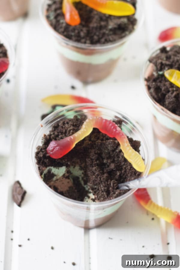 Delicious St. Patrick's Day Dirt Cups layered with mint pudding, green whipped cream, and crushed Oreos, garnished with gummy worms.