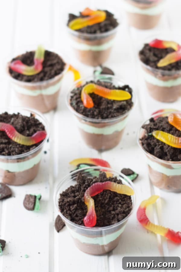 Batch of eight festive St. Patrick's Day Dirt Cups, each individually layered and topped with crushed Oreos and gummy worms, ready for serving.