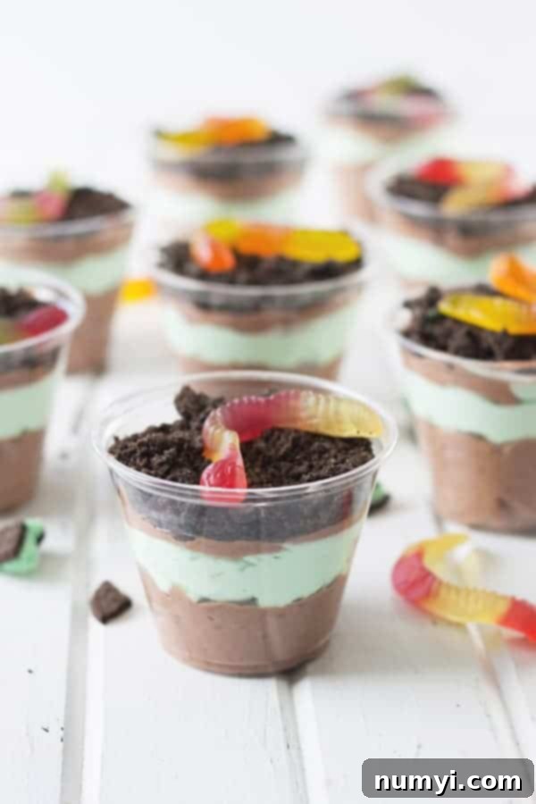 Assortment of St. Patrick's Day Dirt Cups featuring green and brown layers with gummy worms, presented on a clean white surface.