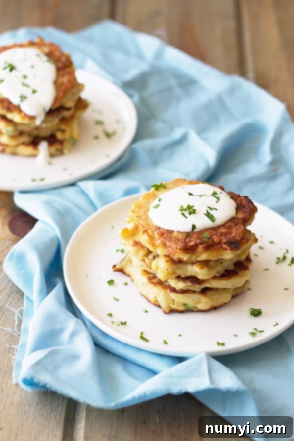 Golden Mashed Potato Fritters 2 Two plates stacked with golden-brown potato scallion pancakes, generously topped with a dollop of sour cream and a sprinkle of fresh green herbs, ready to be served.