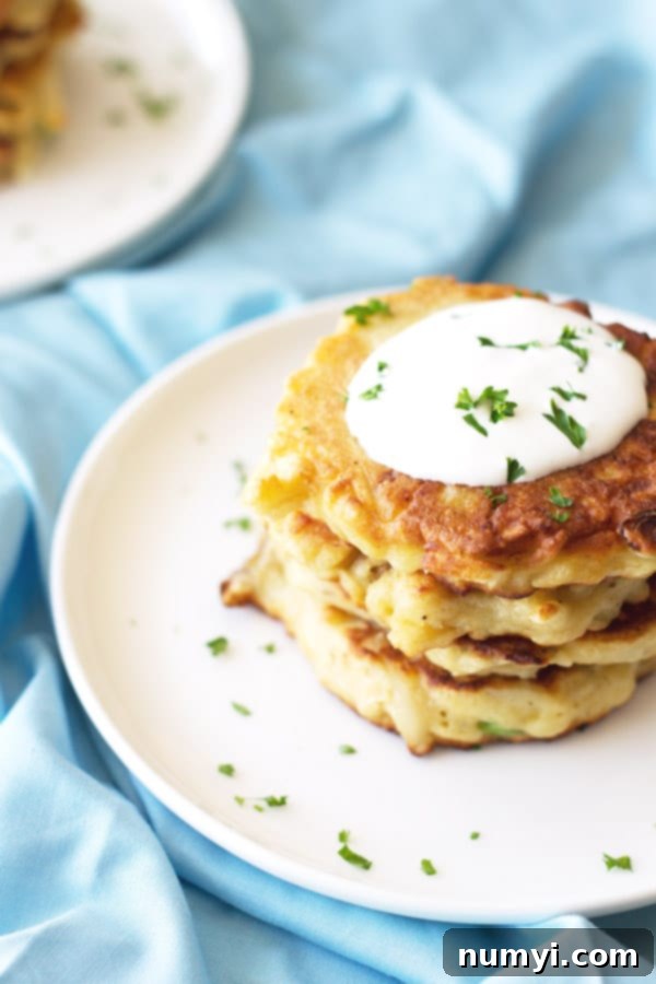 Golden Mashed Potato Fritters 4 An overhead shot of perfectly golden-brown mashed potato scallion pancakes stacked on a pristine white plate, elegantly garnished with fresh herbs and a luxurious swirl of sour cream.