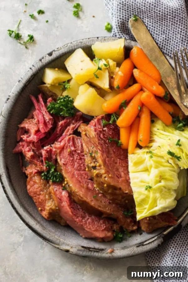 Perfect Slow Cooker Guinness Corned Beef 4 Close-up top down view of a large serving of tender sliced corned beef, with steaming cabbage, carrots, and potatoes, perfectly arranged.