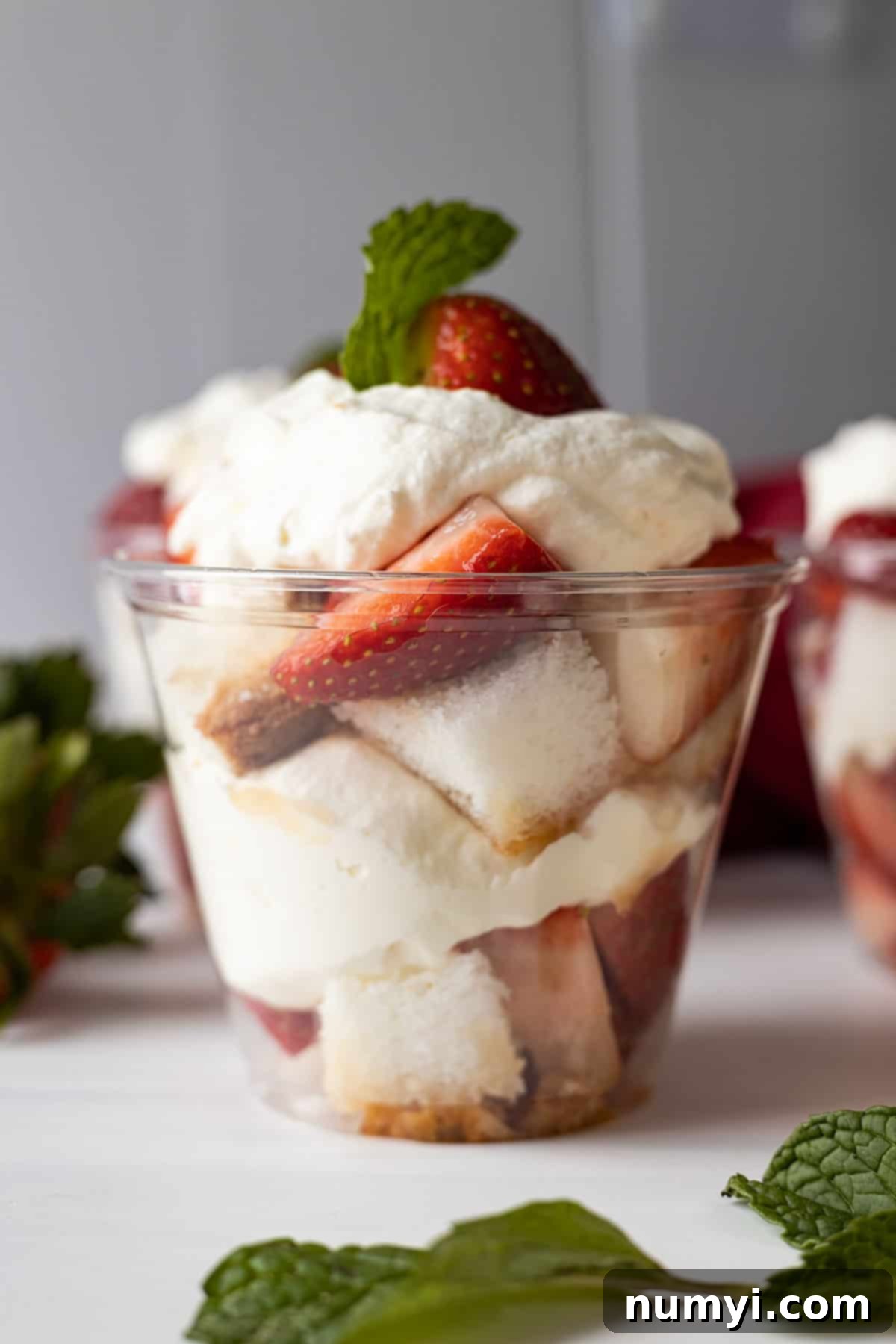 A clear plastic cup layered with angel food cake cubes, fresh strawberries, and freshly whipped cream.