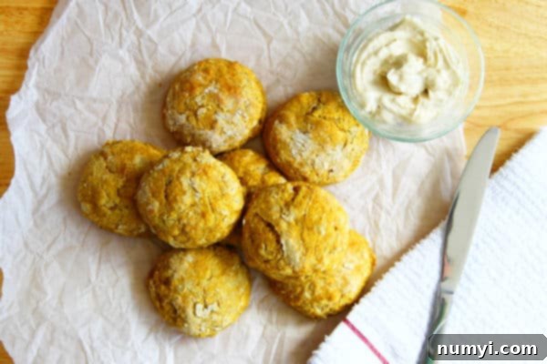 overhead shot of pumpkin biscuits arranged on parchment paper with a glass bowl of maple butter and a knit beside them