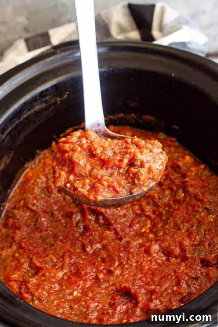 Easy Crock Pot Spaghetti Sauce 4 Close-up overhead shot of a ladle scooping thick, rich slow cooker spaghetti sauce from the crock pot. Steam is rising, highlighting the sauce's hearty consistency.
