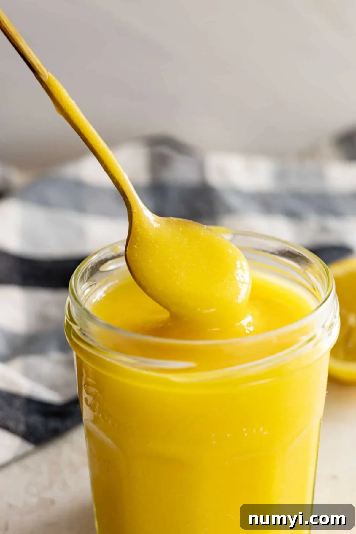 A spoon pulling up lemon curd from the jar. 