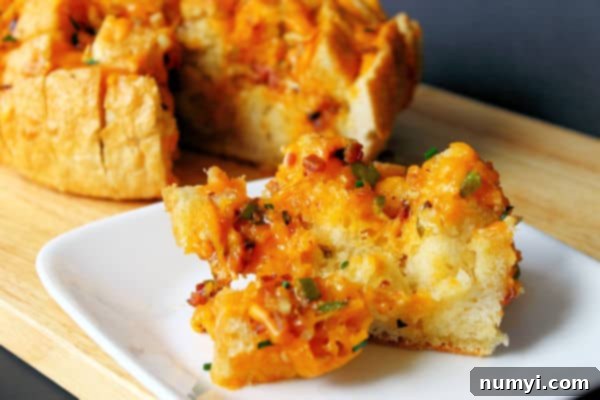 jalapeno cheese bread with bacon pulled apart with one serving on a small white plate in the foreground, showing gooey cheese