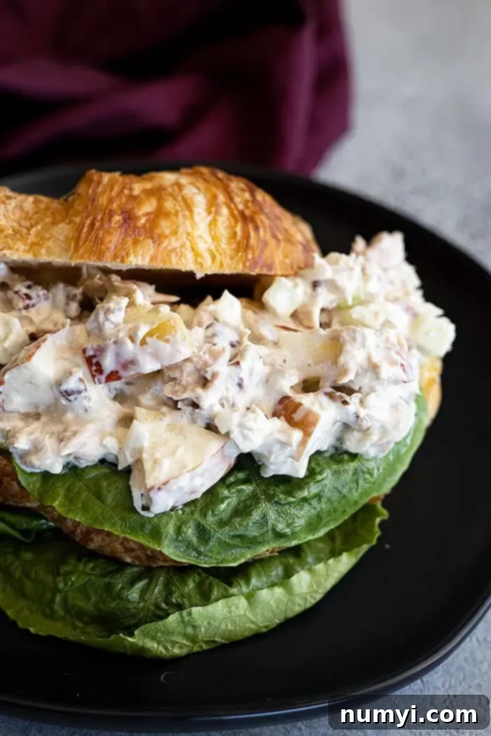 Crisp Apple Tuna Delight 2 Closeup: Tuna salad with apples piled high on a buttery croissant with a fresh lettuce leaf, ready to be enjoyed.