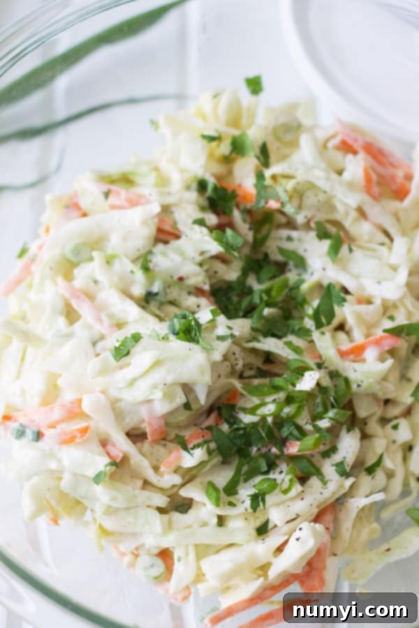 Closeup of vibrant, creamy homemade coleslaw in a clear glass mixing bowl, ready to serve.