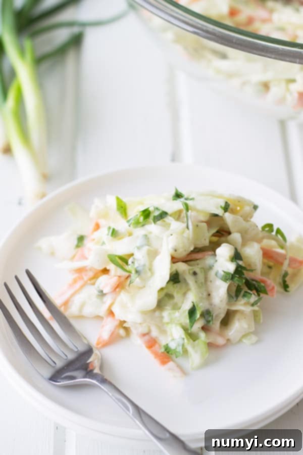 Freshly made shredded cabbage and carrot coleslaw served on a pristine white plate next to a silver fork, highlighting its inviting texture.