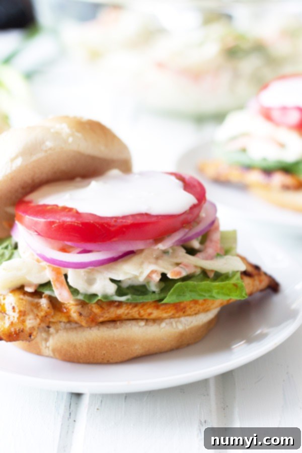 Grilled buffalo chicken sandwich topped with lettuce, tomato, creamy coleslaw, and onion on a bun.