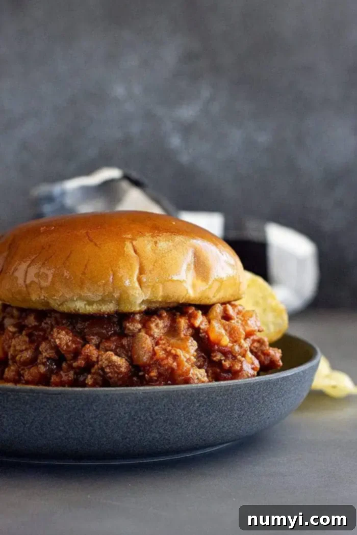 A homemade sloppy joe on a toasted bun with pickles, served on a blue plate, highlighting the rich, savory sauce.
