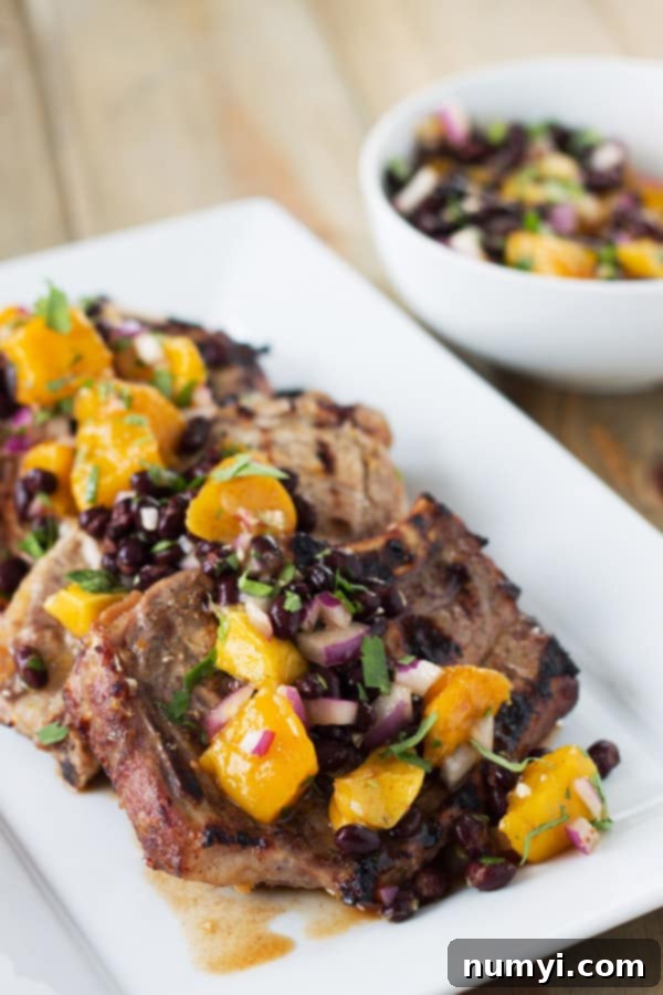 Grilled citrus marinated pork chops topped generously with fresh mango and black bean salsa on a white plate, showcasing the vibrant colors.
