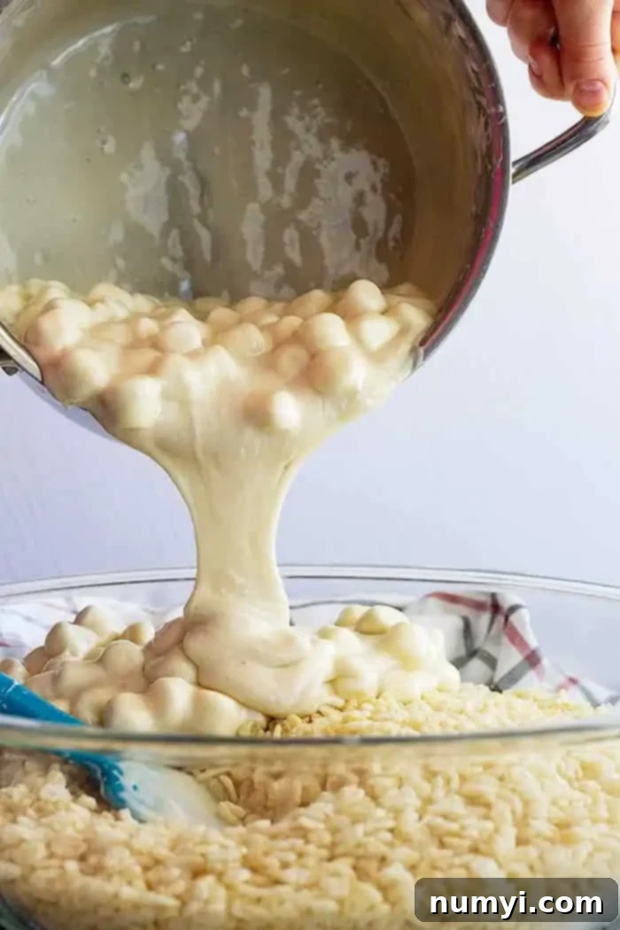 pouring marshmallow mixture into rice krispies in a large pot