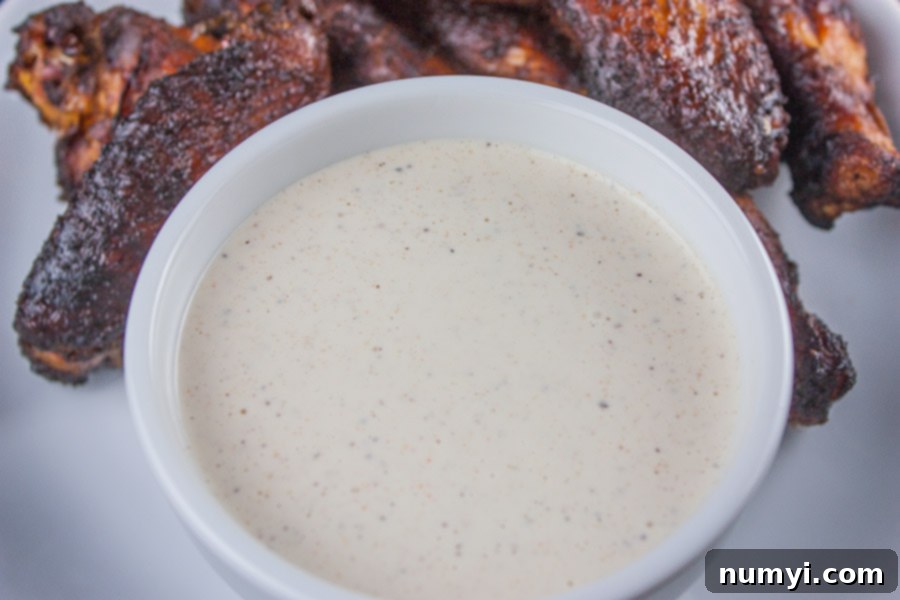 Alabama White BBQ Sauce in a white ramekin, surrounded by perfectly smoked chicken wings.