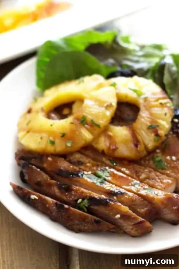 closeup: a teriyaki pork chop on a plate with two slices of grilled pineapple on top with a fresh green salad to the side