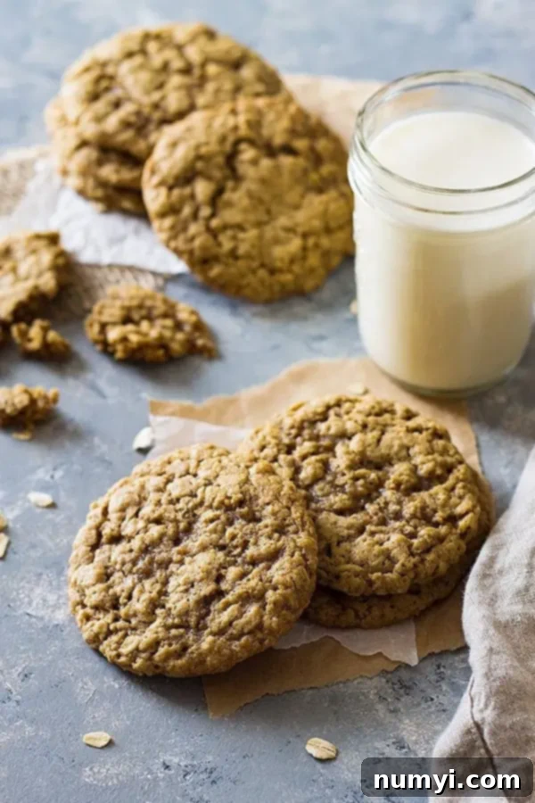 Three soft and chewy oatmeal cookies, one with a bite taken out, arranged with a glass of milk.