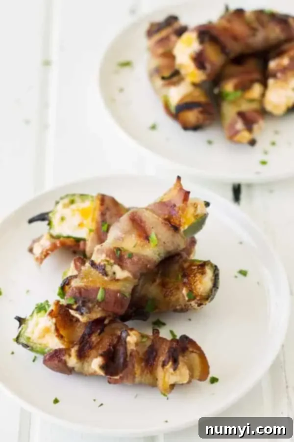 Grilled Jalapeño Poppers with creamy cheese mixture and crispy bacon on a white plate, garnished with herbs.