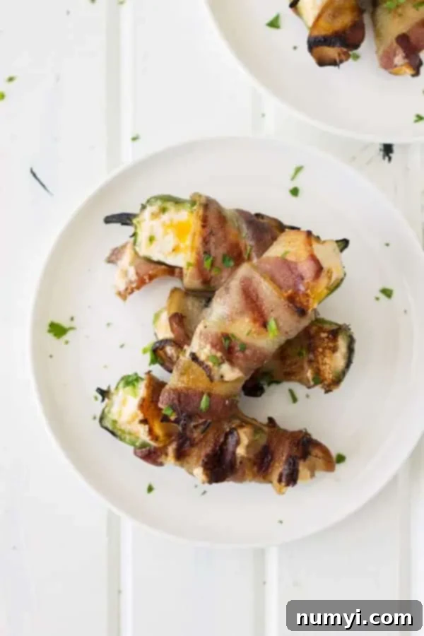 Overhead view of several grilled jalapeno poppers with melted cheese and crispy bacon on a white serving plate.