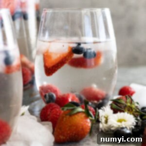 A glass of easy white sangria ready to drink. Ice cubes and fresh fruit all around the glas.