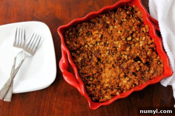 Healthy apple crisp served in a red square baking dish, next to an empty white plate with two forks, ready to be enjoyed.