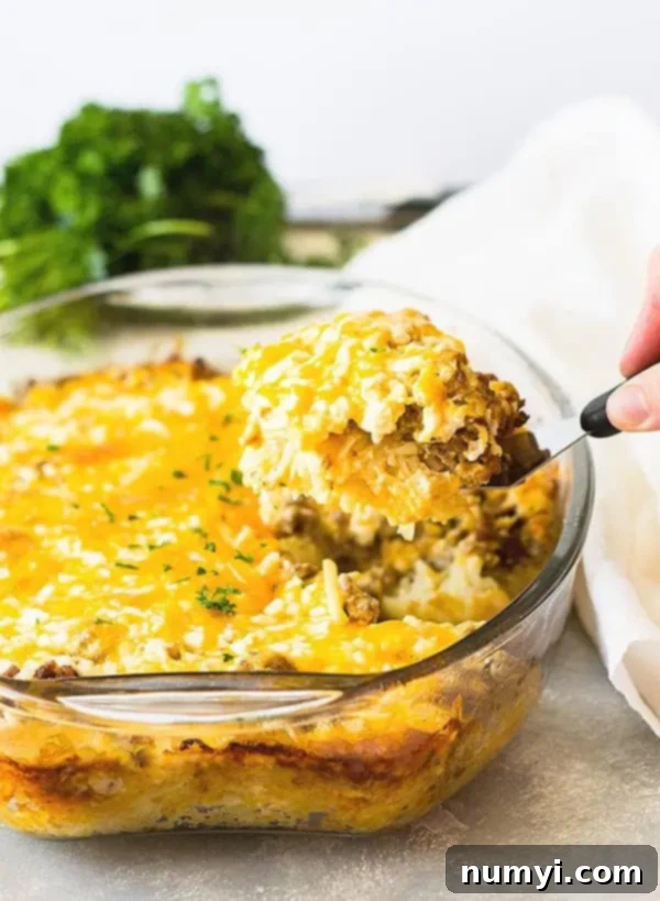 side view: a spatula lifting a perfectly golden piece of hash brown casserole with eggs and sausage out of the baking dish