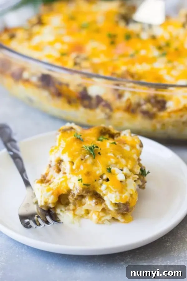 a piece of breakfast sausage casserole with hash browns on a small white plate with a metal fork, ready to be eaten