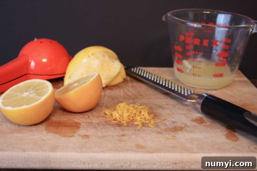 Close-up of a golden Meyer Lemon Loaf, showing its beautiful texture and the shiny glaze, alongside fresh Meyer lemons and their zest on a wooden board.