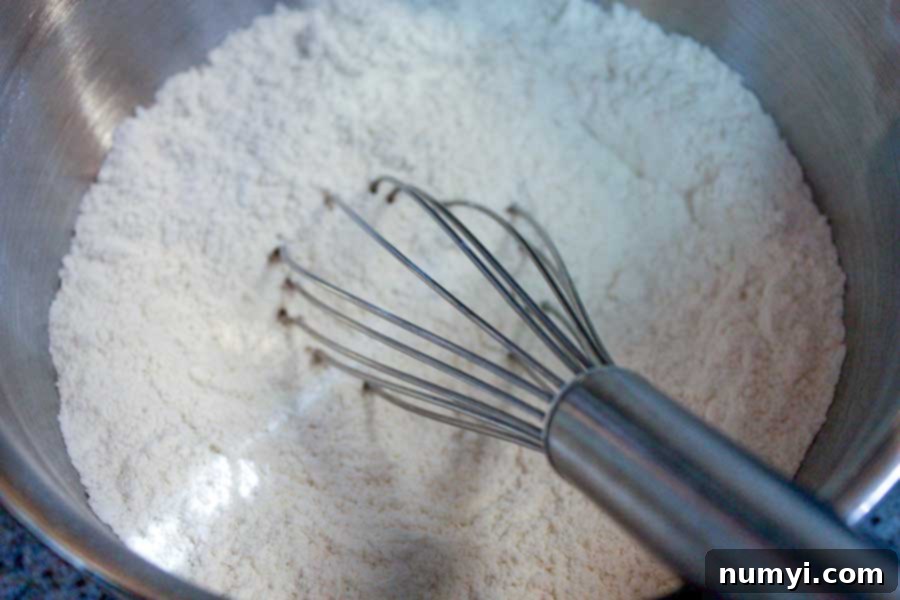 Dry ingredients for Meyer Lemon Loaf – flour, baking powder, and salt – meticulously combined in a sleek metal bowl, ready for the wet mixture.