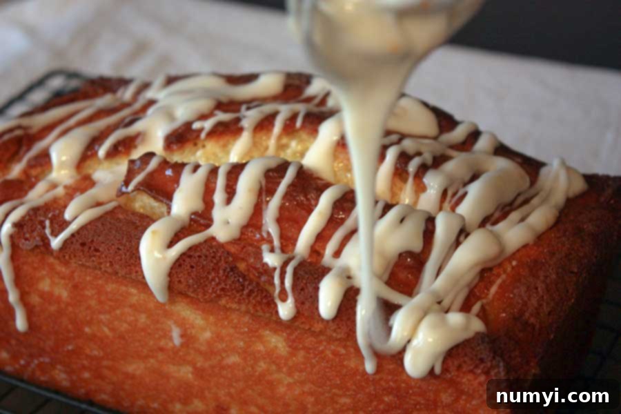 A smooth, bright lemon icing being expertly drizzled over the cooled Meyer Lemon Loaf, creating an inviting cascade of sweetness.