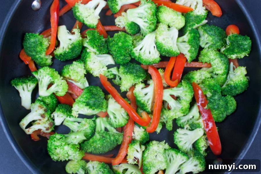 Easy Chicken and Broccoli Stir Fry - broccoli and red bell peppers being stir-fried in a skillet pan