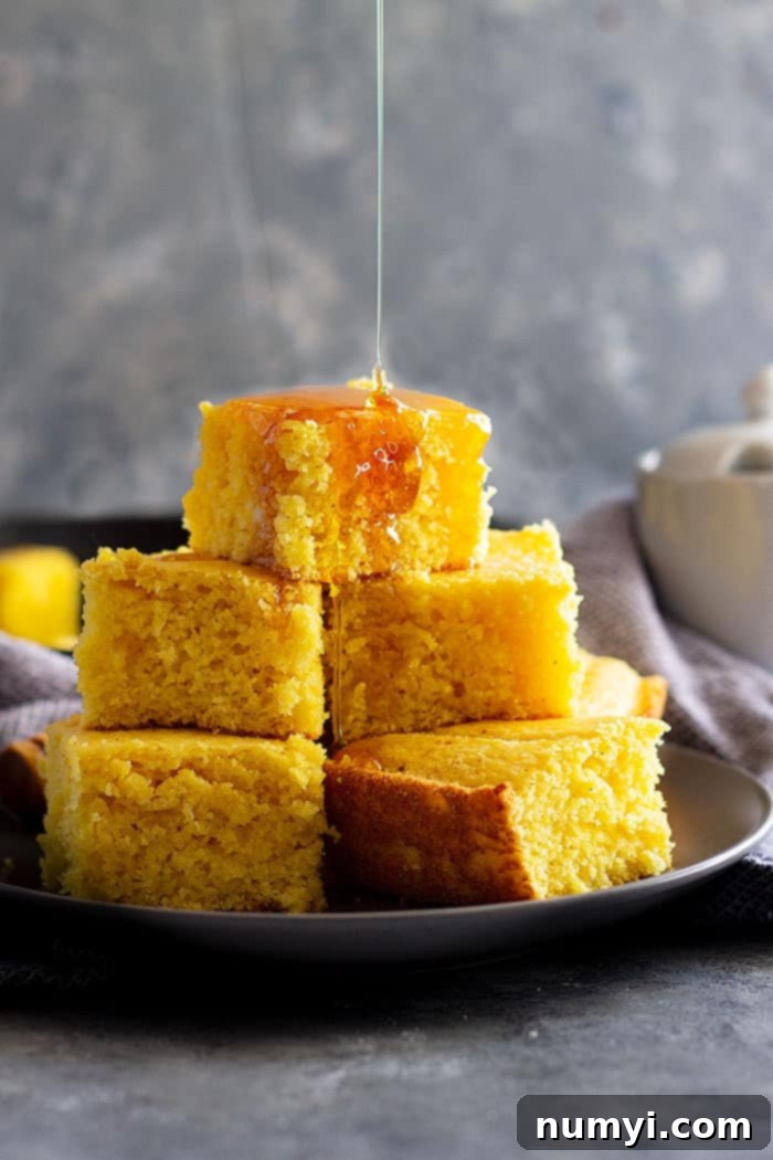 Plate with a slice of golden buttermilk cornbread being drizzled in sweet honey.