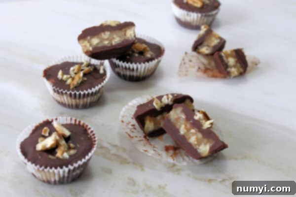 Chocolate Pecan Pie Bites scattered on a light marbled surface with a couple of them cut open to reveal the pecan pie filling, showing the rich interior and smooth chocolate exterior