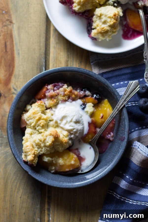 Close-up of a generous scoop of homemade Blueberry Peach Cobbler with a fluffy biscuit topping, served in a bowl, steam gently rising.