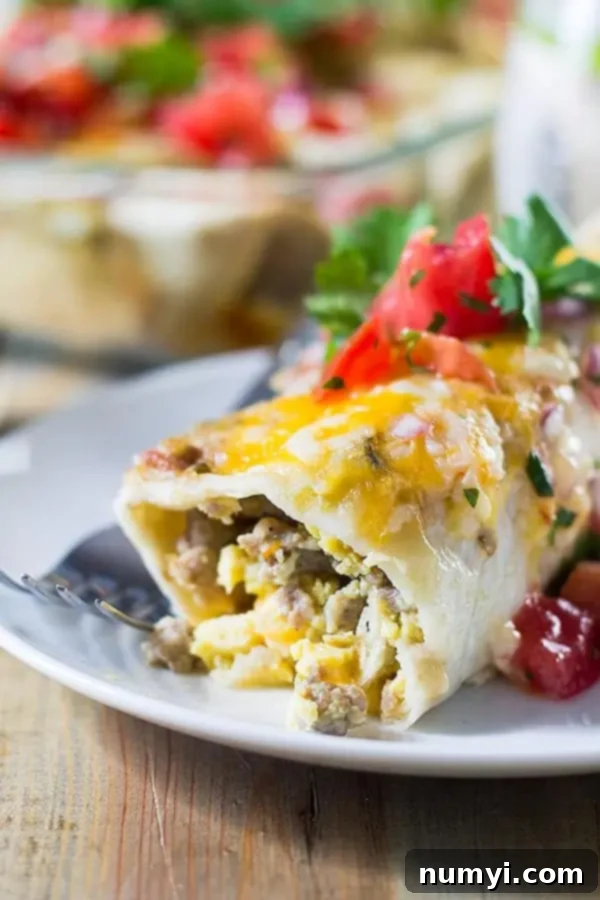 side view closeup: egg enchiladas filled with sausage, scrambled eggs, and green chiles, topped with melted cheese.