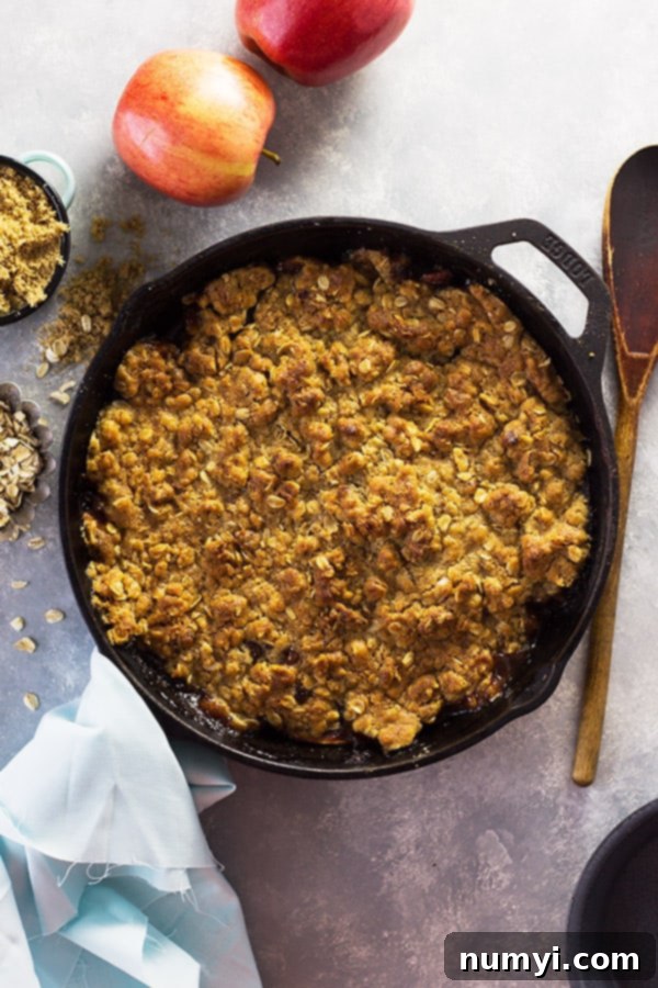 A close-up shot of a golden-brown, bubbly Easy Apple Butter Apple Crisp in a cast iron skillet, with sweet tender apples and a crunchy oat topping.