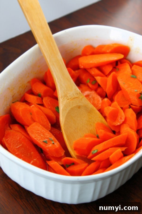 Beautifully arranged ginger maple glazed carrots in a white serving dish with a wooden spoon, ready to be served.