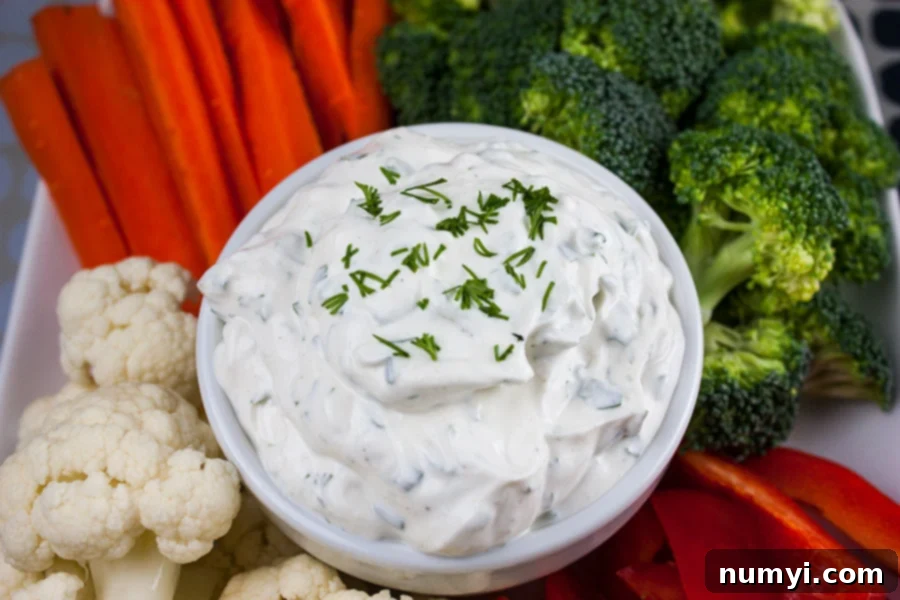 Fresh Herb Vegetable Dip in a white bowl surrounded by cut broccoli, cauliflower, carrots, and red bell pepper