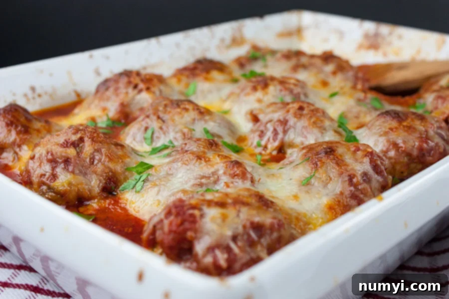 Baked Parmesan Meatballs in white casserole pan with marinara sauce and melted cheese.