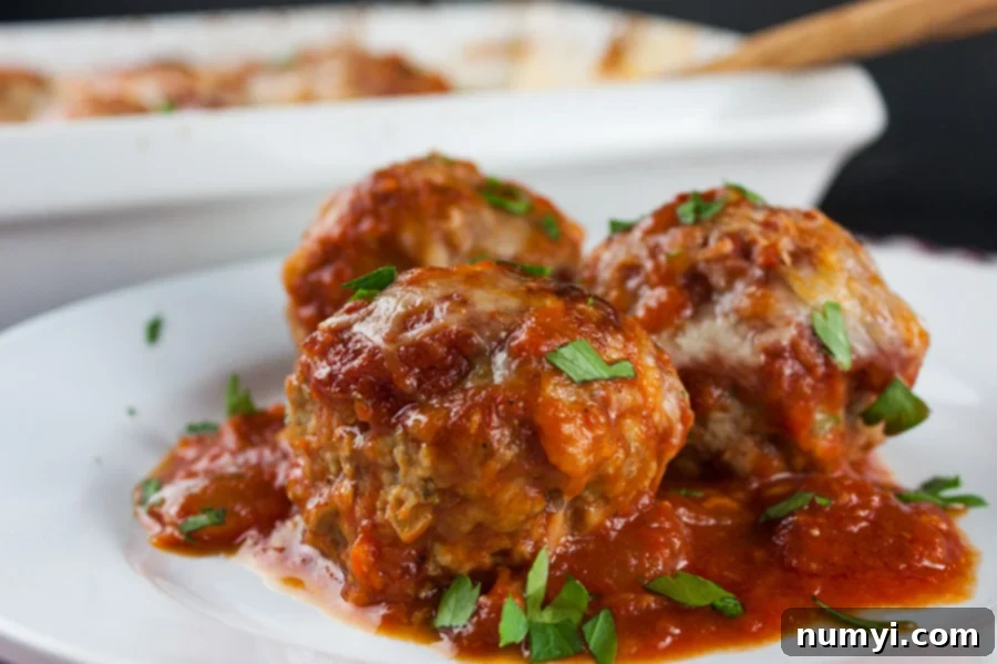 three Baked Parmesan Meatballs on white plate garnished with sauce and chopped parsley