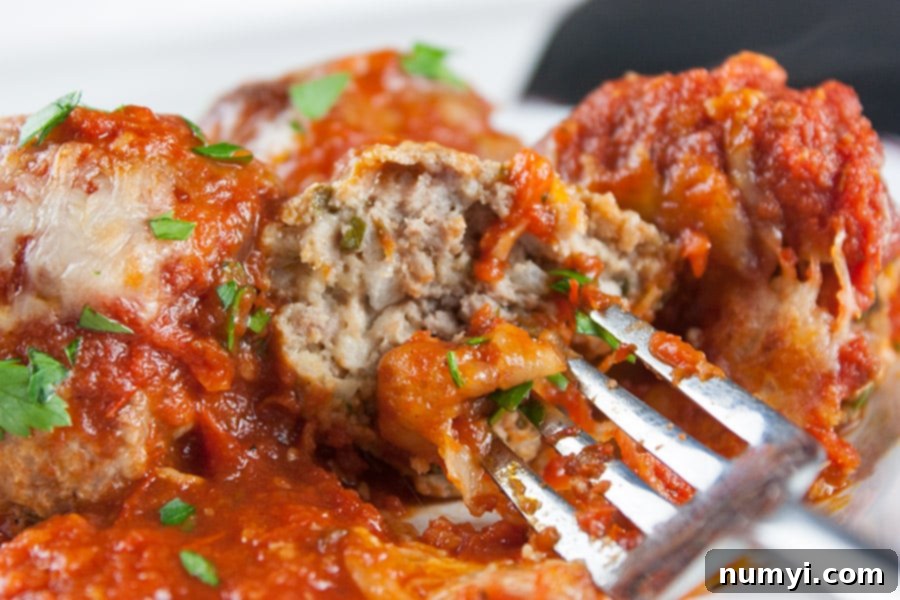 close up of Baked Parmesan Meatballs one cut open on a fork, showing the tender interior.