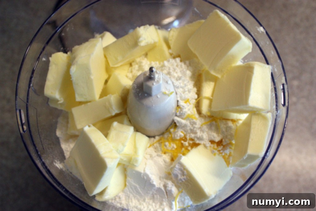 Unsalted butter cubes and all-purpose flour in the bowl of a food processor, ready to be blended for cookie dough.